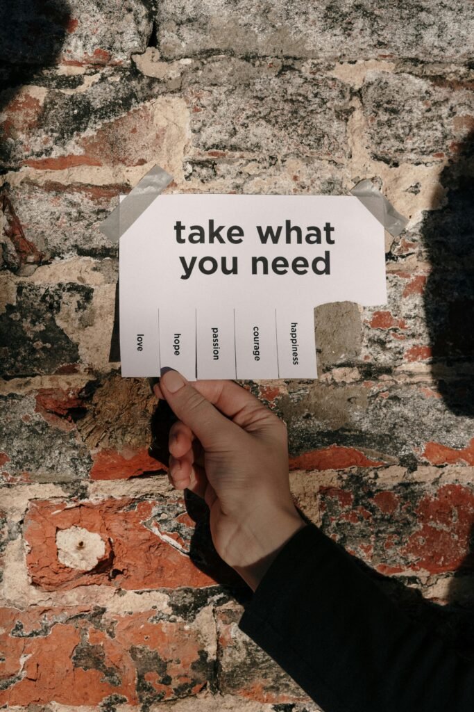 A hand holds a tear-off note with inspirational text against a brick wall, offering words like hope, love, courage.